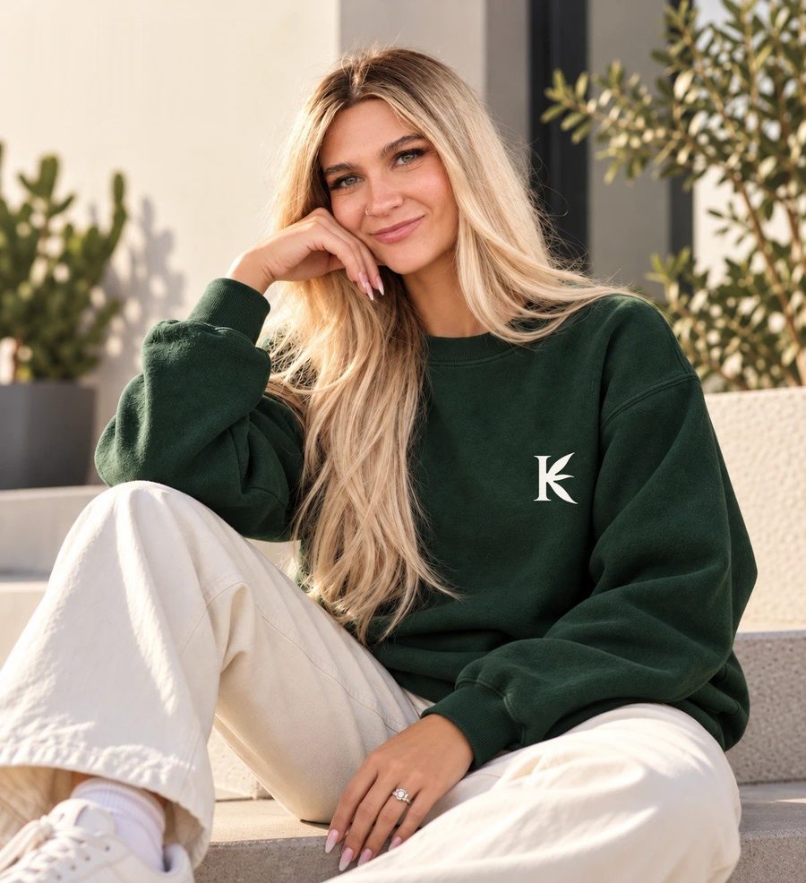 Concept image: a woman in the forest Signature Crewneck, sitting on sunlit steps. The leaf K was added to the photo digitally.